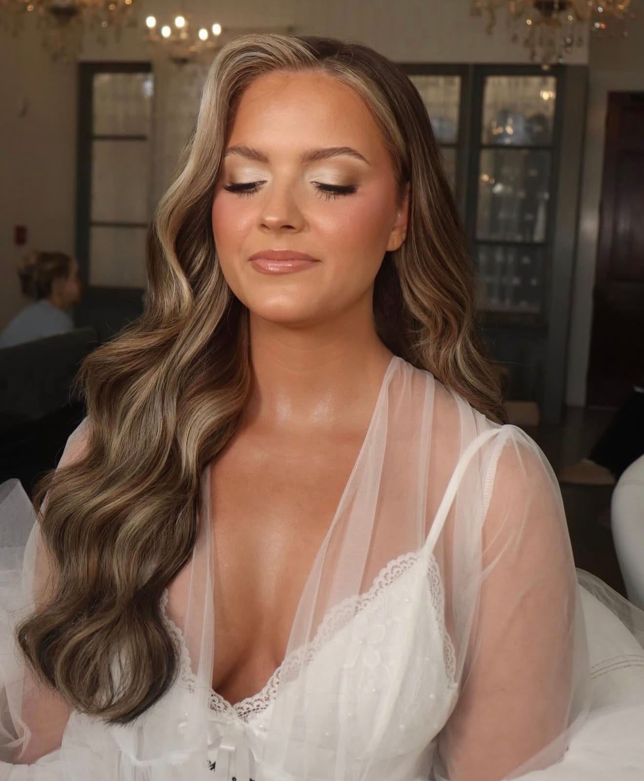 Bride in a tulle robe with a champagne shimmer eye, under chandelier light